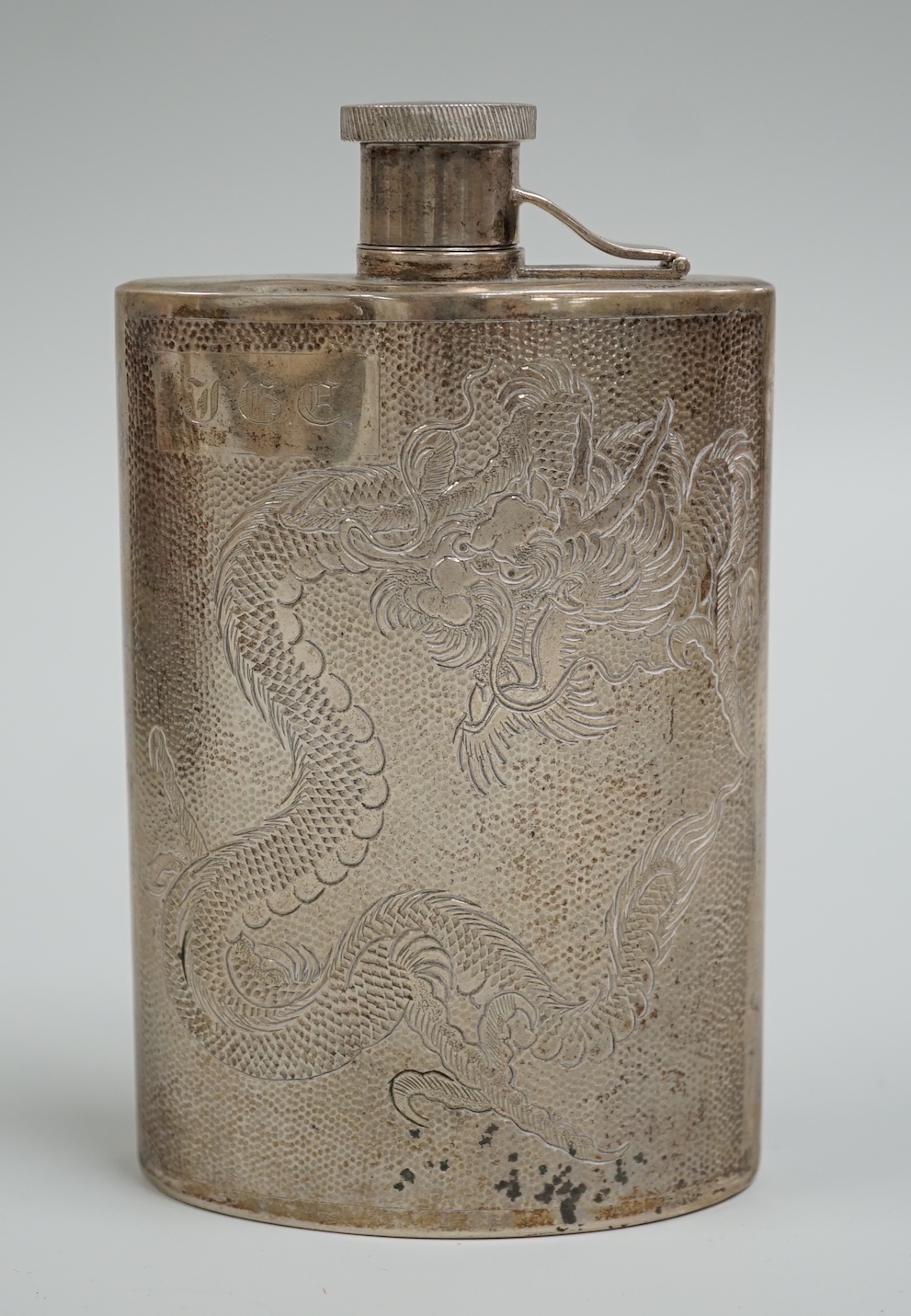 An early 20th century Chinese white metal hip flask, engraved with dragon, inscription and initials, 14.5oz, 6.7oz.